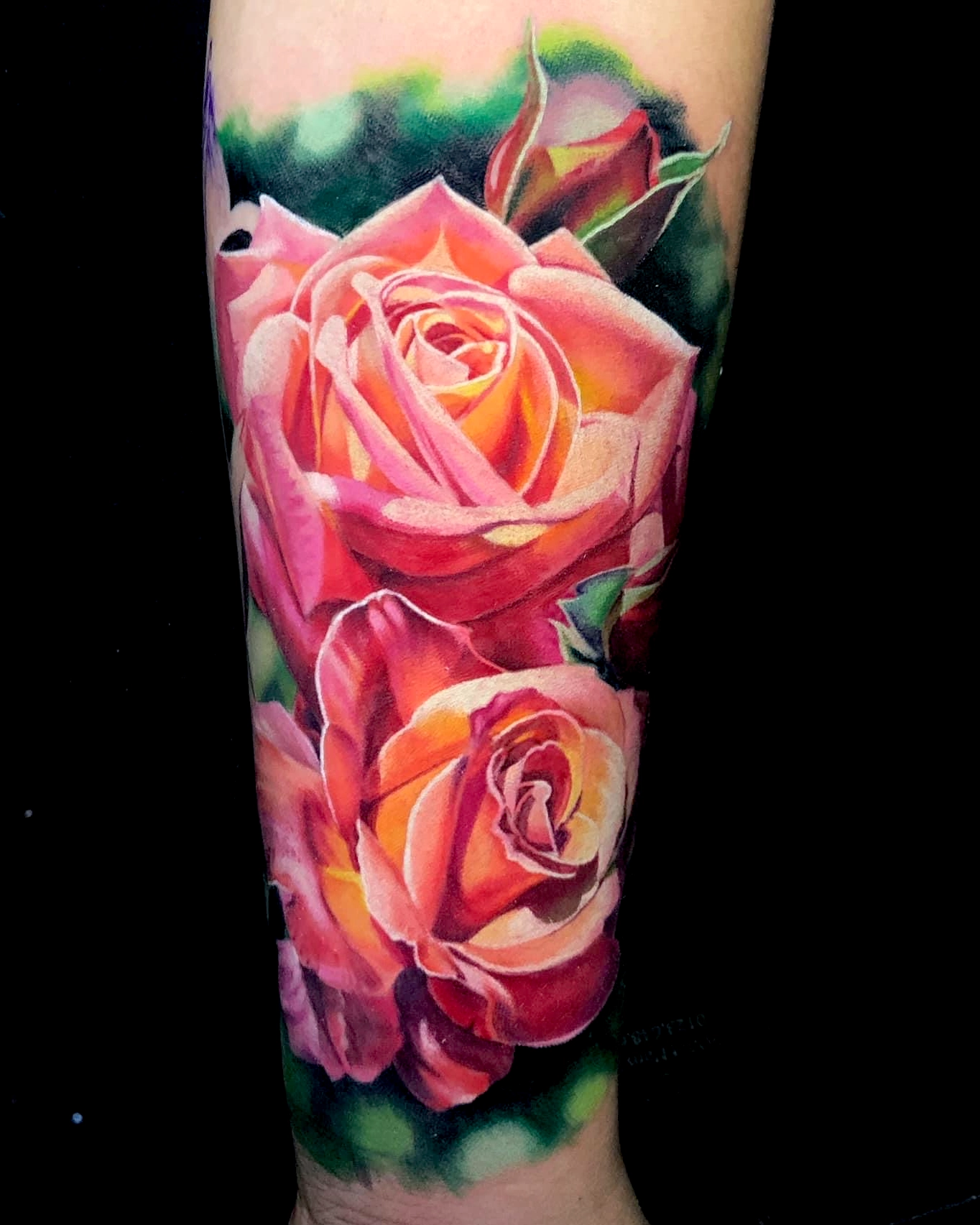 Color realism forearm tattoo featuring two pink and orange roses with green foliage by Quang Pham at Qneedle Tattoo Studio